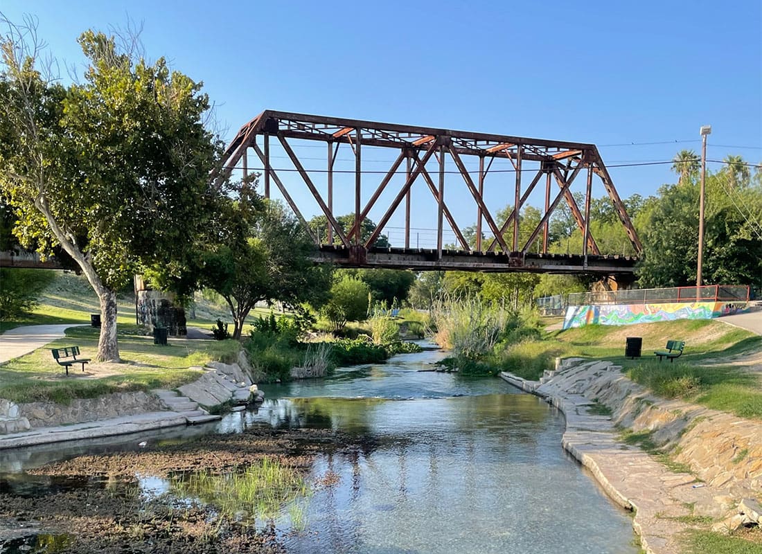 Contact - Scenic Landscape of a Steel Bridge Across a Shallow River Surrounded by Green Grass and Trees in Del Rio Texas